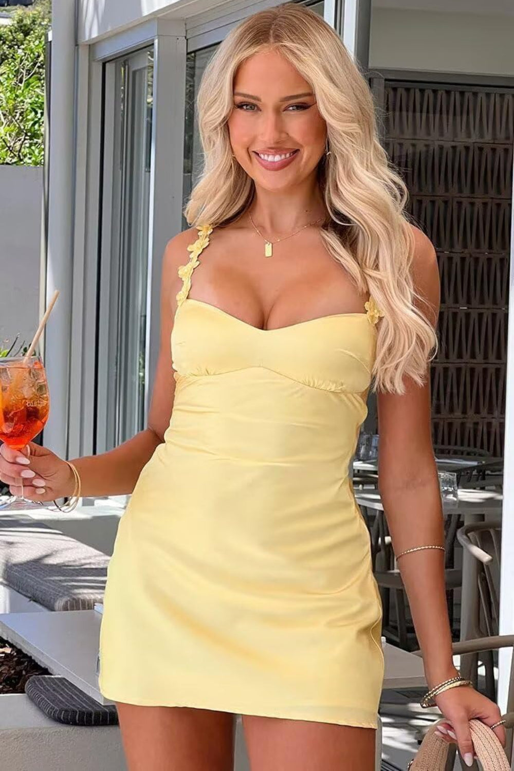 Satin Homecoming Dresses yellow satin mini dress with floral straps modeled by smiling blonde woman holding a cocktail on patio