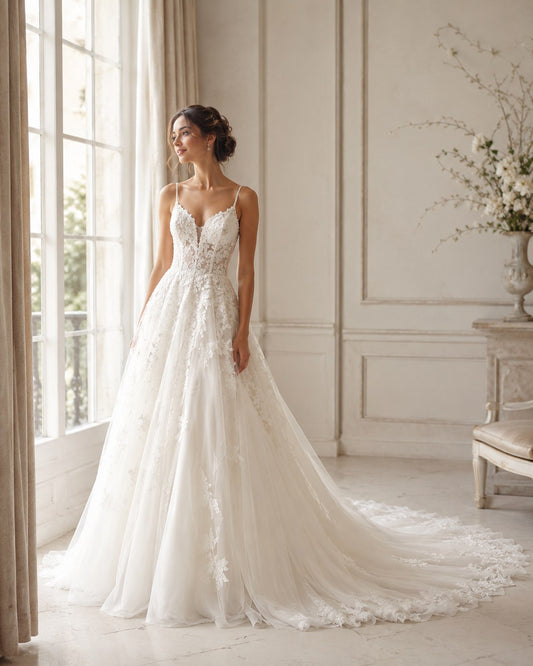 Bride in a white lace A-line wedding dress by a sunlit window