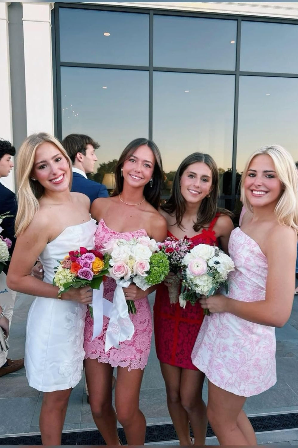 Four smiling young women in short lace and floral gowns holding bouquets for dance Floral Homecoming Dresses from 27dress
