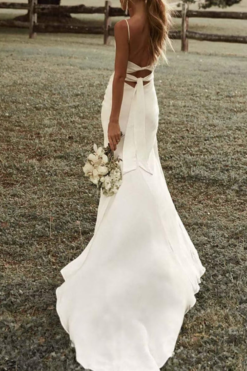 Back of a white spaghetti-strap bridal gown with tie details and a long train.